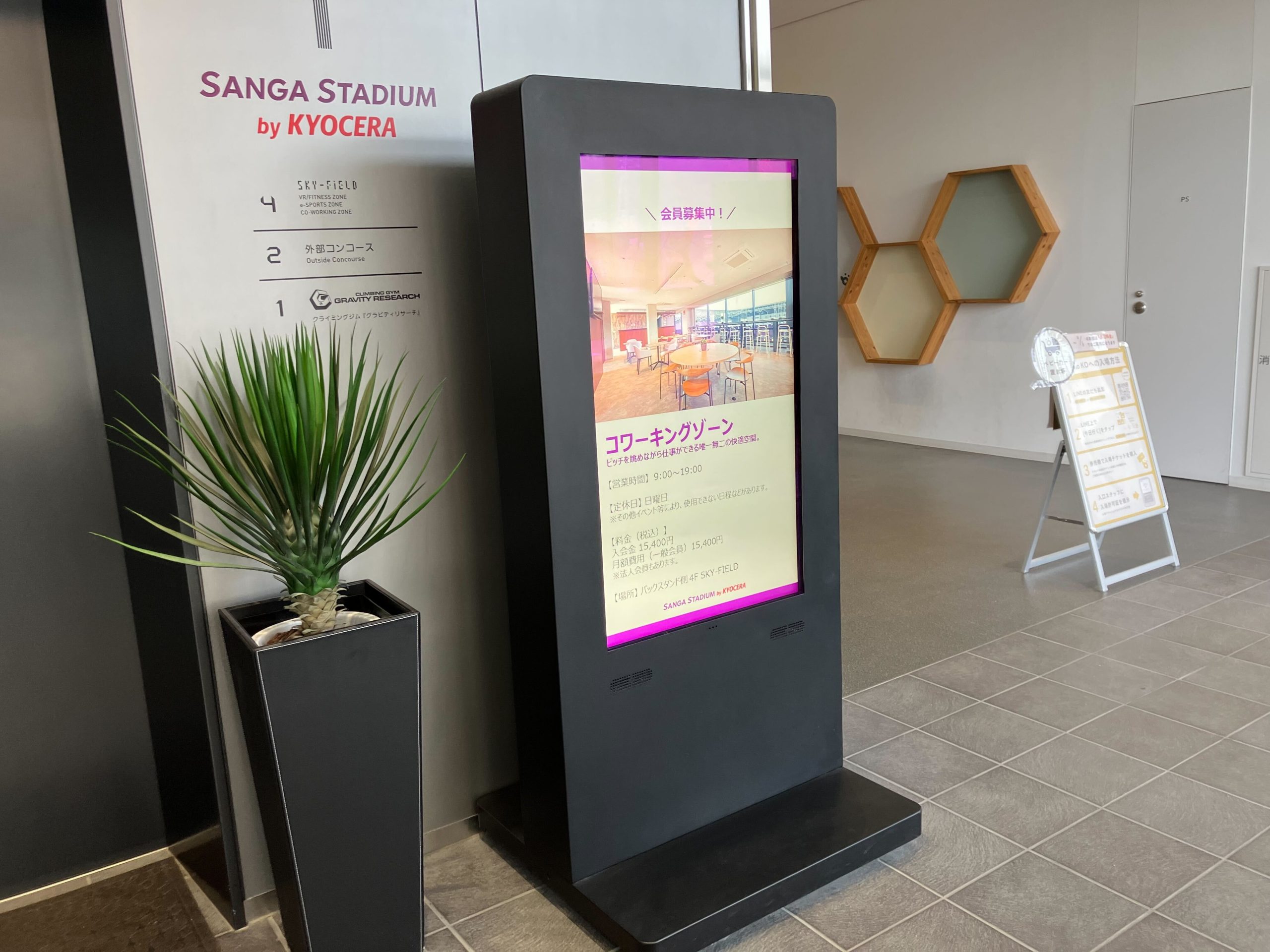 SANGA STADIUM by KYOCERAの屋内施設入口に設置されたデジタルサイネージ。キャスター付きで移動可能な設計が確認できる。