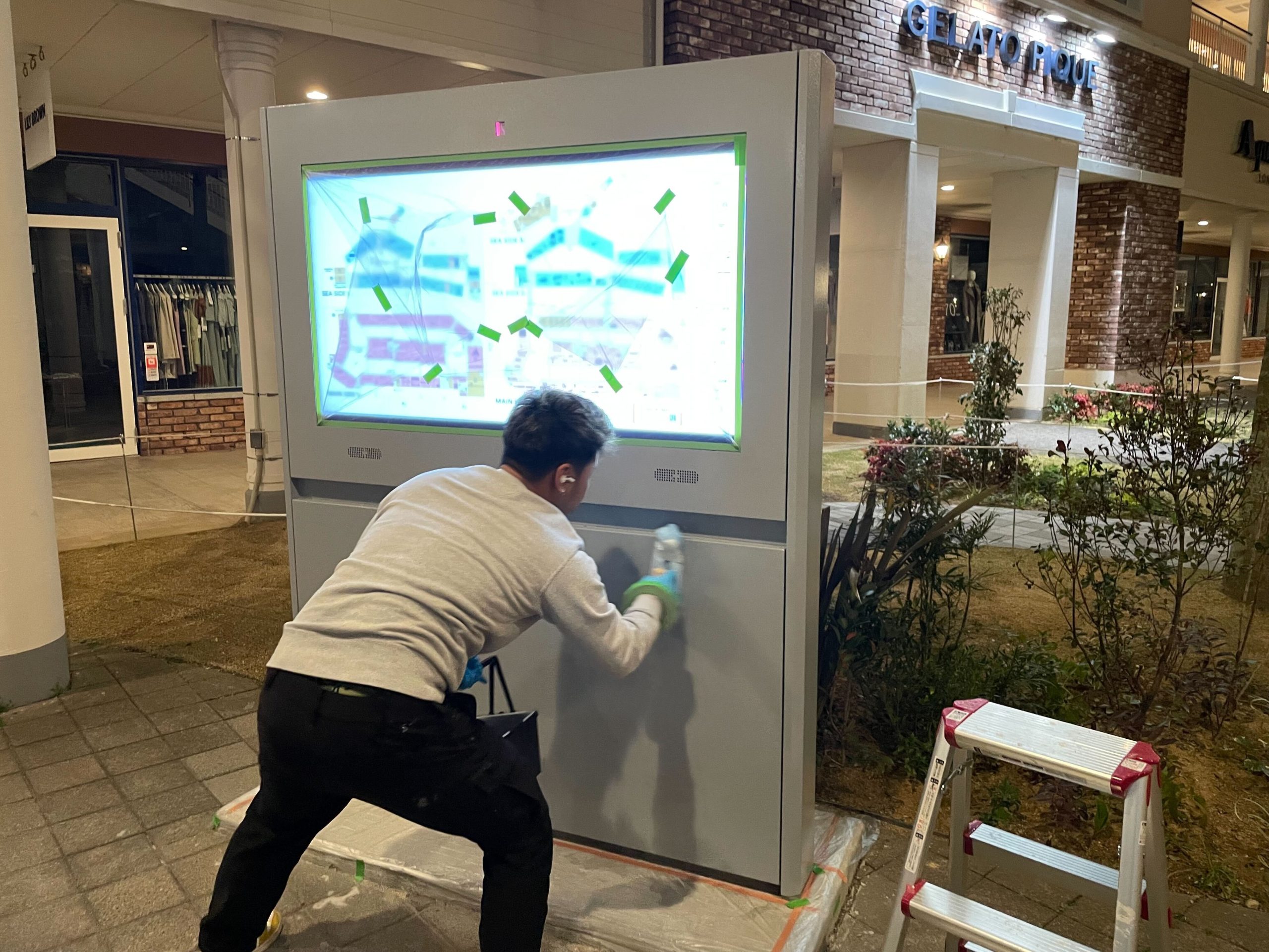 アウトレットモール内に屋外デジタルサイネージ（H557SDV）を設置する様子。作業員が丁寧に設置作業を行っている夜間施工の風景。